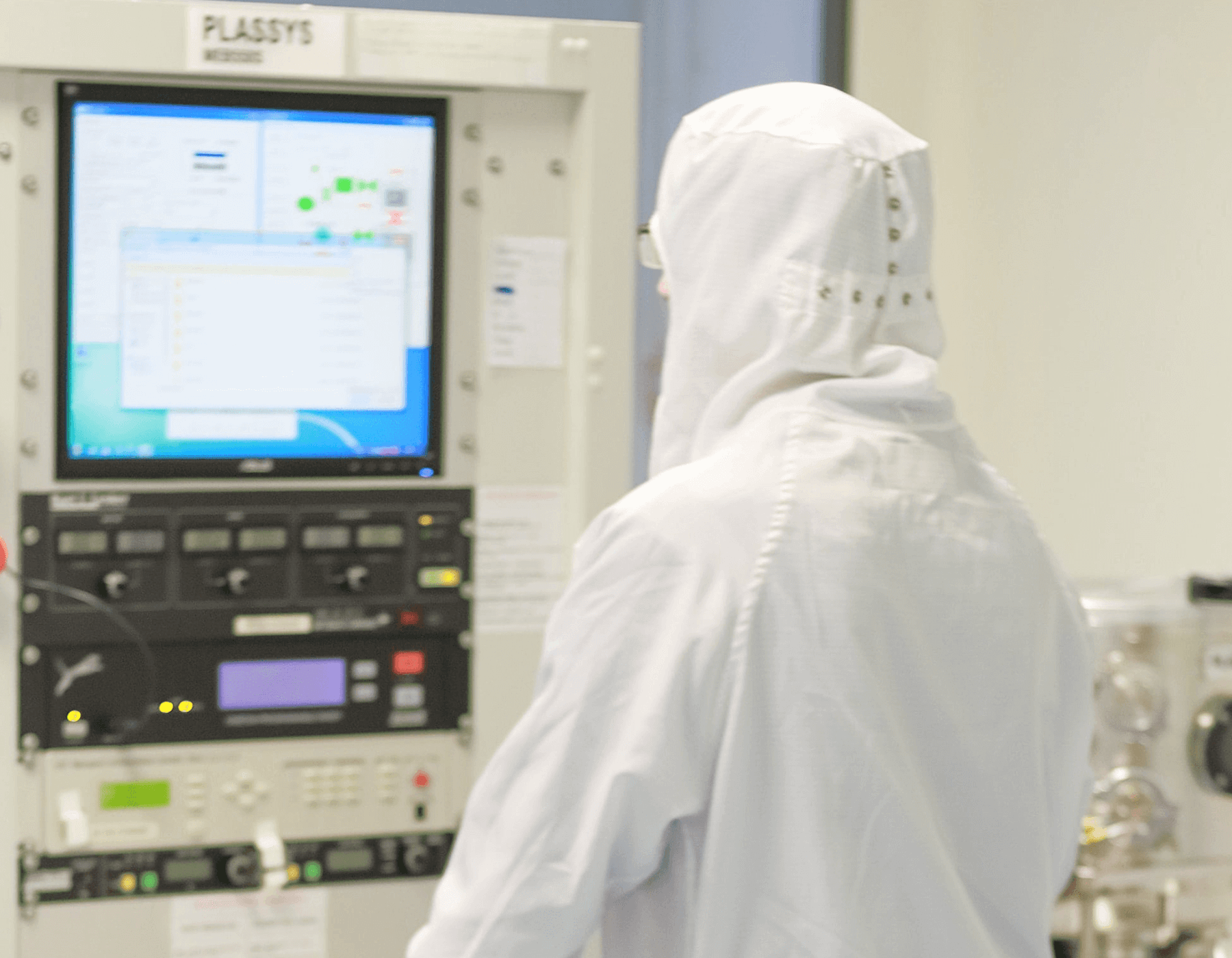 Technician in a cleanroom hood monitoring an equipment control panel