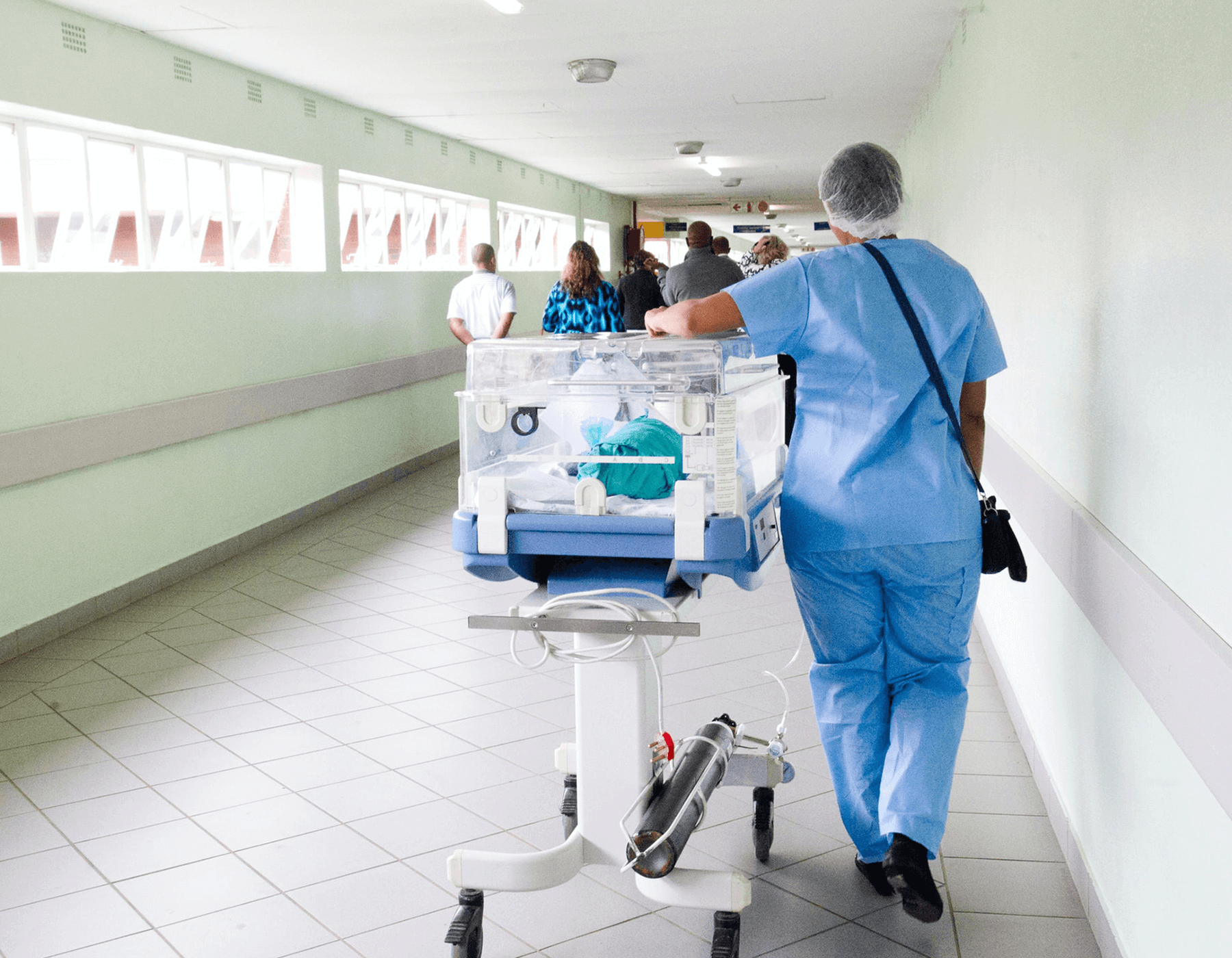 Nurse wheeling an infant incubator down a hospital corridor